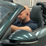 Noé Serrano en un Jaguar descapotable de lujo en el taller mecánico para ilustrar la realidad de ganar dinero con inteligencia artificial.