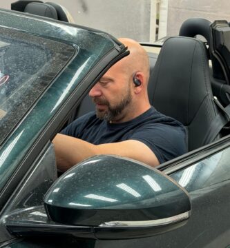 Noé Serrano en un Jaguar descapotable de lujo en el taller mecánico para ilustrar la realidad de ganar dinero con inteligencia artificial.