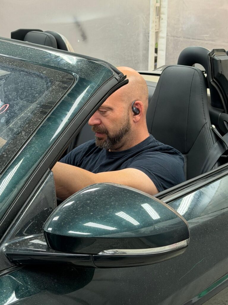 Noé Serrano en un Jaguar descapotable de lujo en el taller mecánico para ilustrar la realidad de ganar dinero con inteligencia artificial.