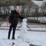 Noé Serrano sonriendo junto a un muñeco de nieve en un paisaje invernal en Alemania