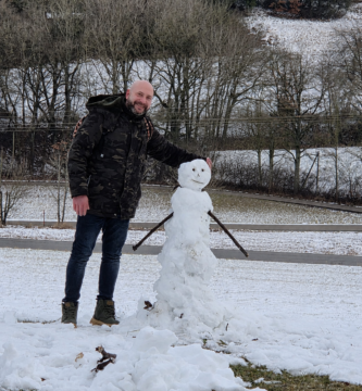 Noé Serrano sonriendo junto a un muñeco de nieve en un paisaje invernal en Alemania