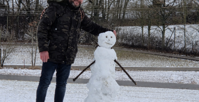 Noé Serrano sonriendo junto a un muñeco de nieve en un paisaje invernal en Alemania