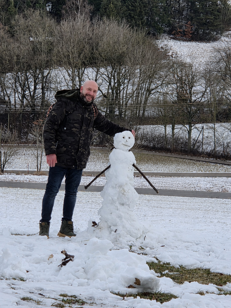 Noé Serrano sonriendo junto a un muñeco de nieve en un paisaje invernal en Alemania