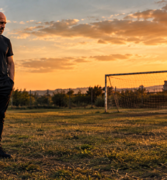 Noé Serrano de pie y solo en un campo de fútbol modesto al atardecer, con un balón a los pies, representando la metáfora de la Intertoto sobre mantener la constancia sin ver resultados