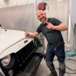 Noé Serrano sonriendo y señalando a cámara en la cabina de pintura de su taller en Alemania