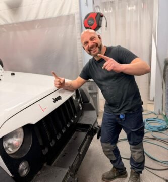 Noé Serrano sonriendo y señalando a cámara en la cabina de pintura de su taller en Alemania