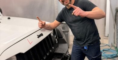 Noé Serrano sonriendo y señalando a cámara en la cabina de pintura de su taller en Alemania