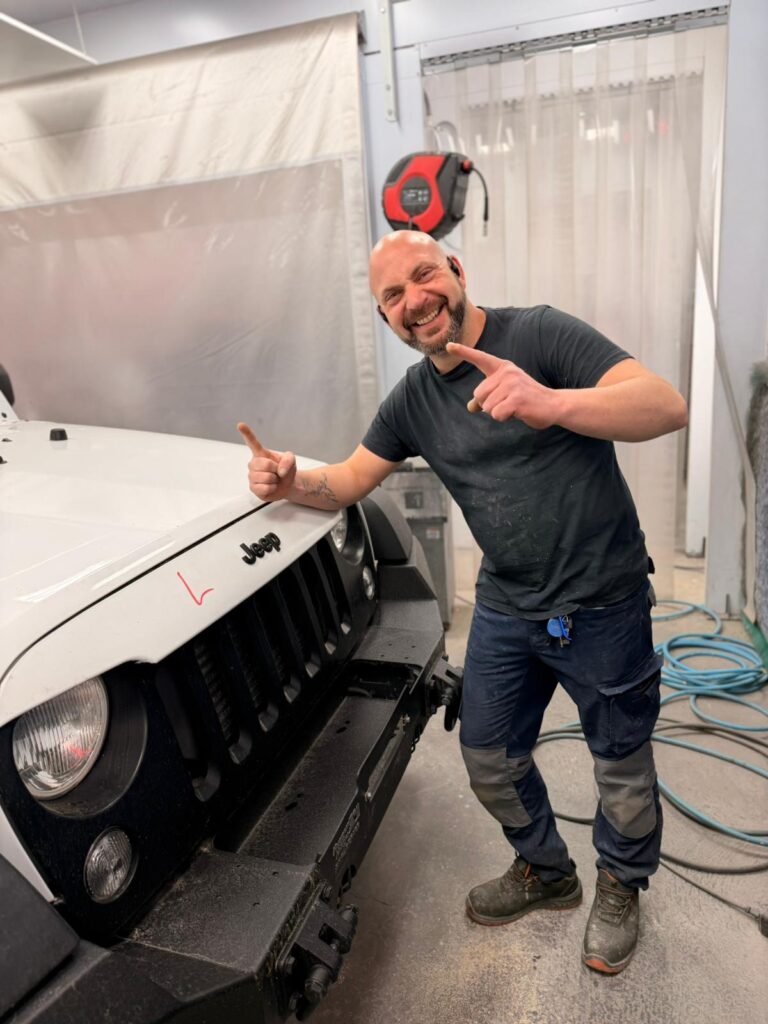 Noé Serrano sonriendo y señalando a cámara en la cabina de pintura de su taller en Alemania
